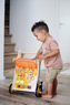 Kind mit orangenem Lauflernwagen aus Holz