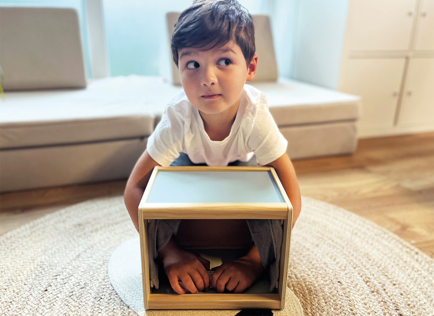 Ein Kind sitzt konzentriert vor einer Fühlbox aus Holz und erfühlt einen Gegenstand