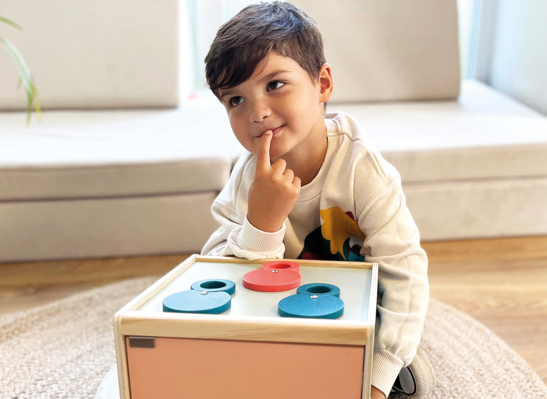 Nachdenklicher Junge sitzt vor einer Sinnesbox und ertastet einen Gegenstand